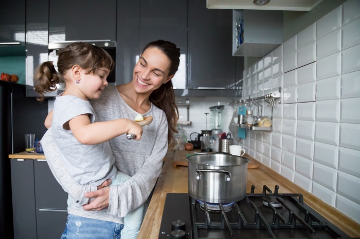 Smiling mom holding kid daughter curious about cooking in kitche